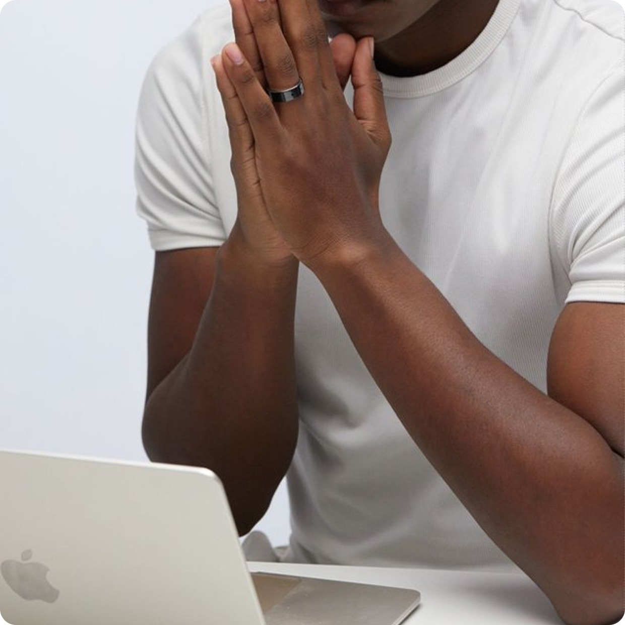 Man pausing, hands folded over laptop